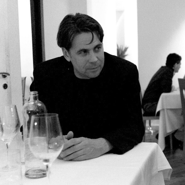 A photograph of a man seated at a table looking askance.