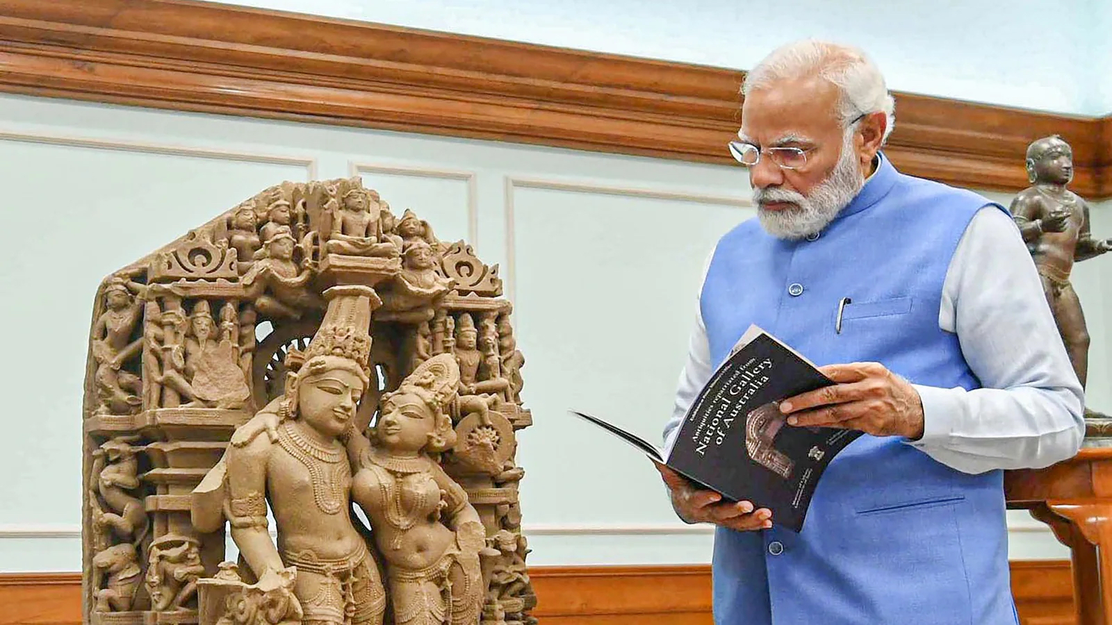 Indian Prime Minister Narendra Modi inspects a sculpture, while holding a catalogue