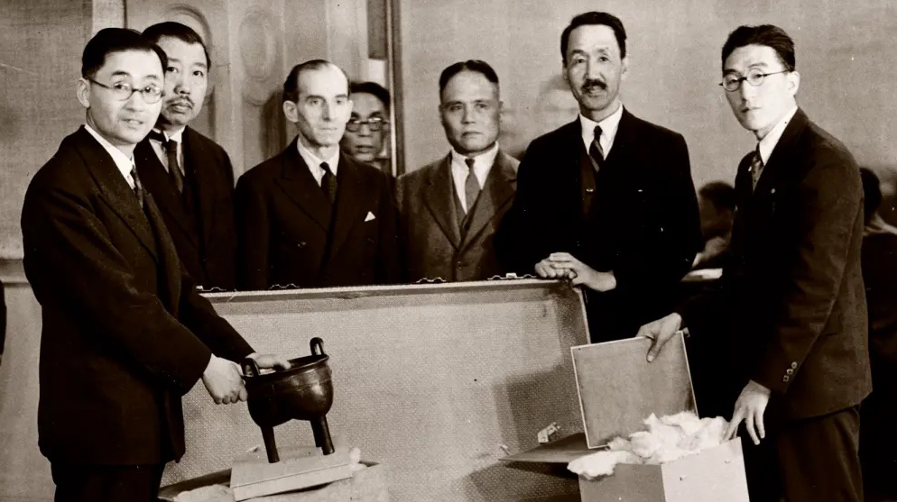 A group of men including Percival David stand in front of open box marked "Handle with Care".