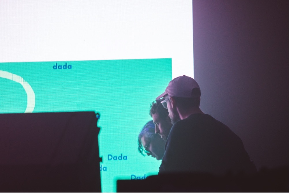 A photograph of Joel Stern, Sean Dockray and James Parker performing in front of a screen.