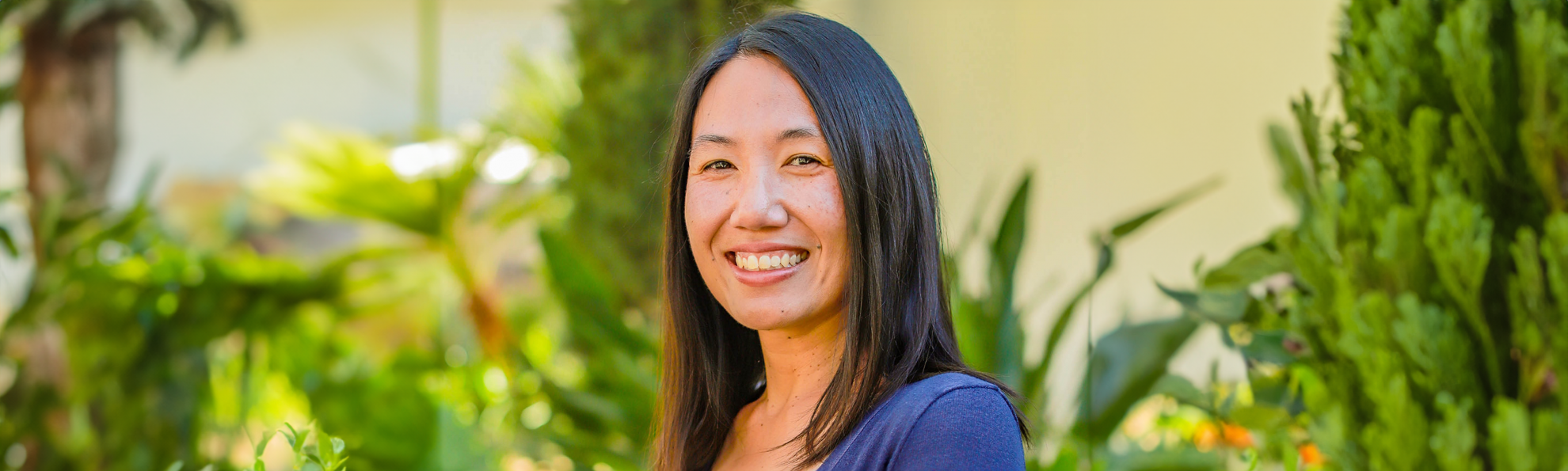 a woman with black hair and a blue top smiles at the camera