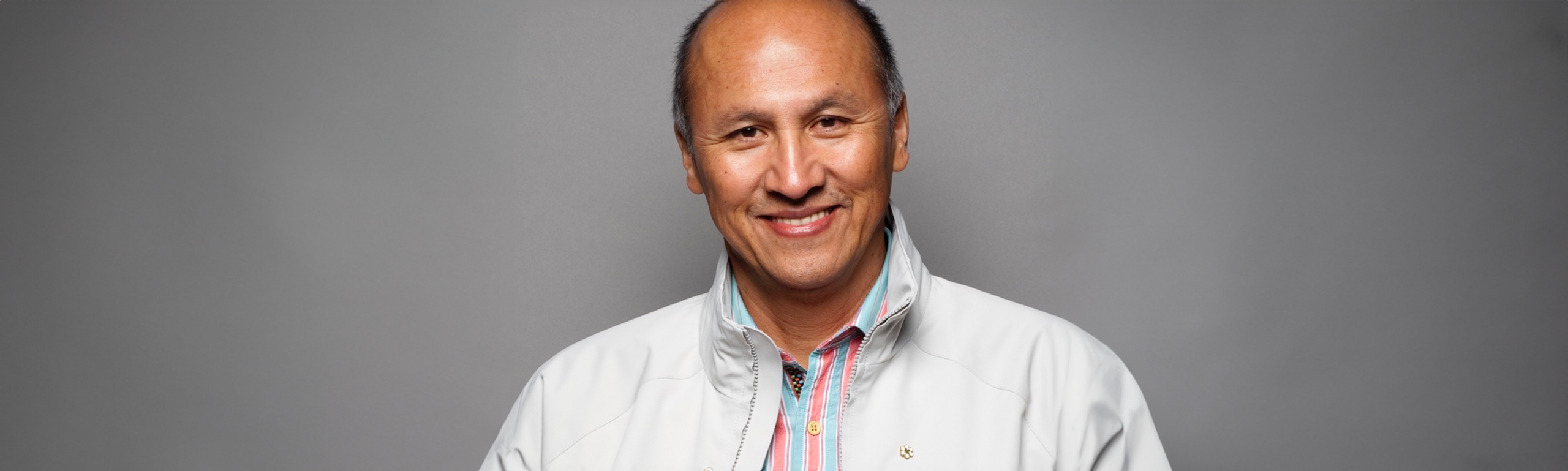 Gerald McMaster stands facing the camera, wearing a white jacket.